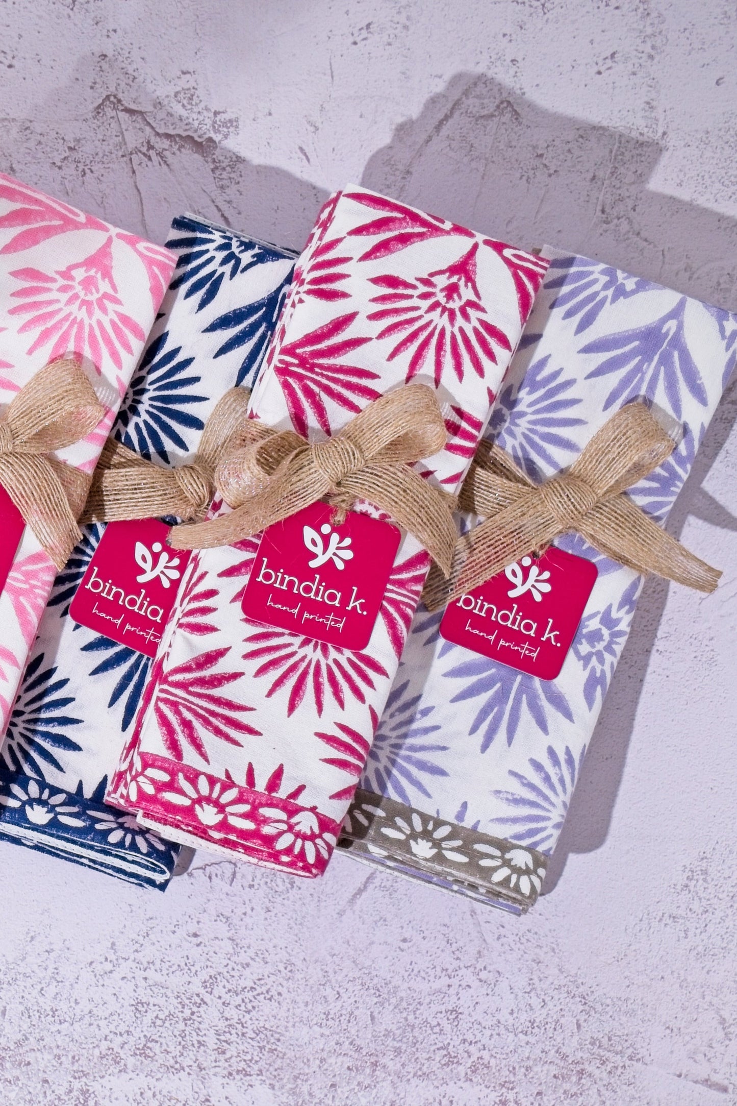 Set of folded napkins with floral patterns and brand labels on a textured surface