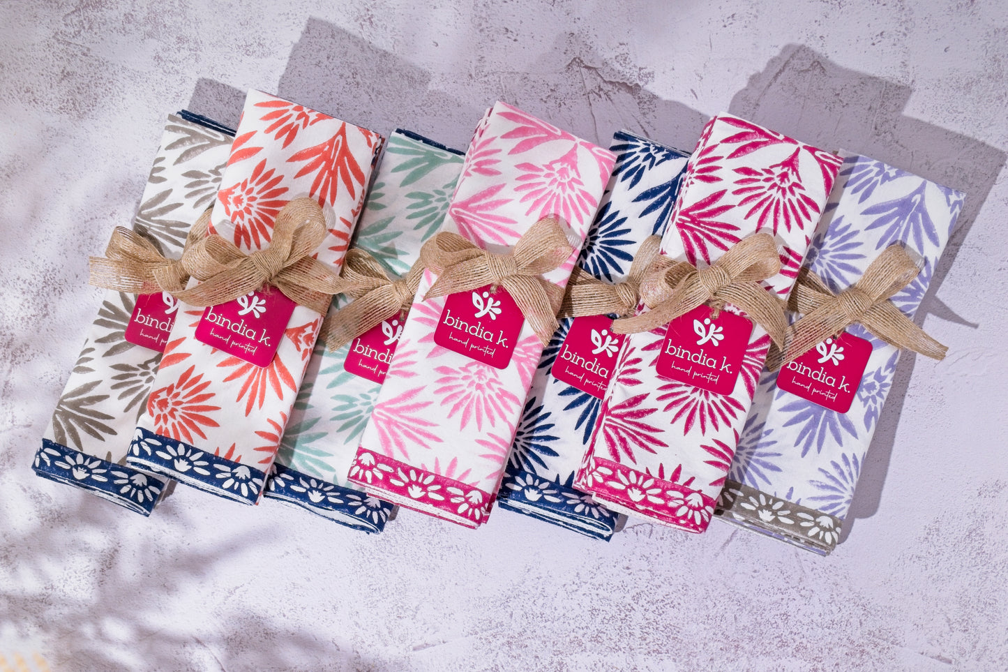 Set of folded cotton napkins with floral patterns and brand labels on a textured surface